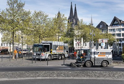 Auf dem Heumarkt in Köln mit dem Dom im Hintergrund stehen eine AWB Kehrmaschine und ein AWB Müllauto. 